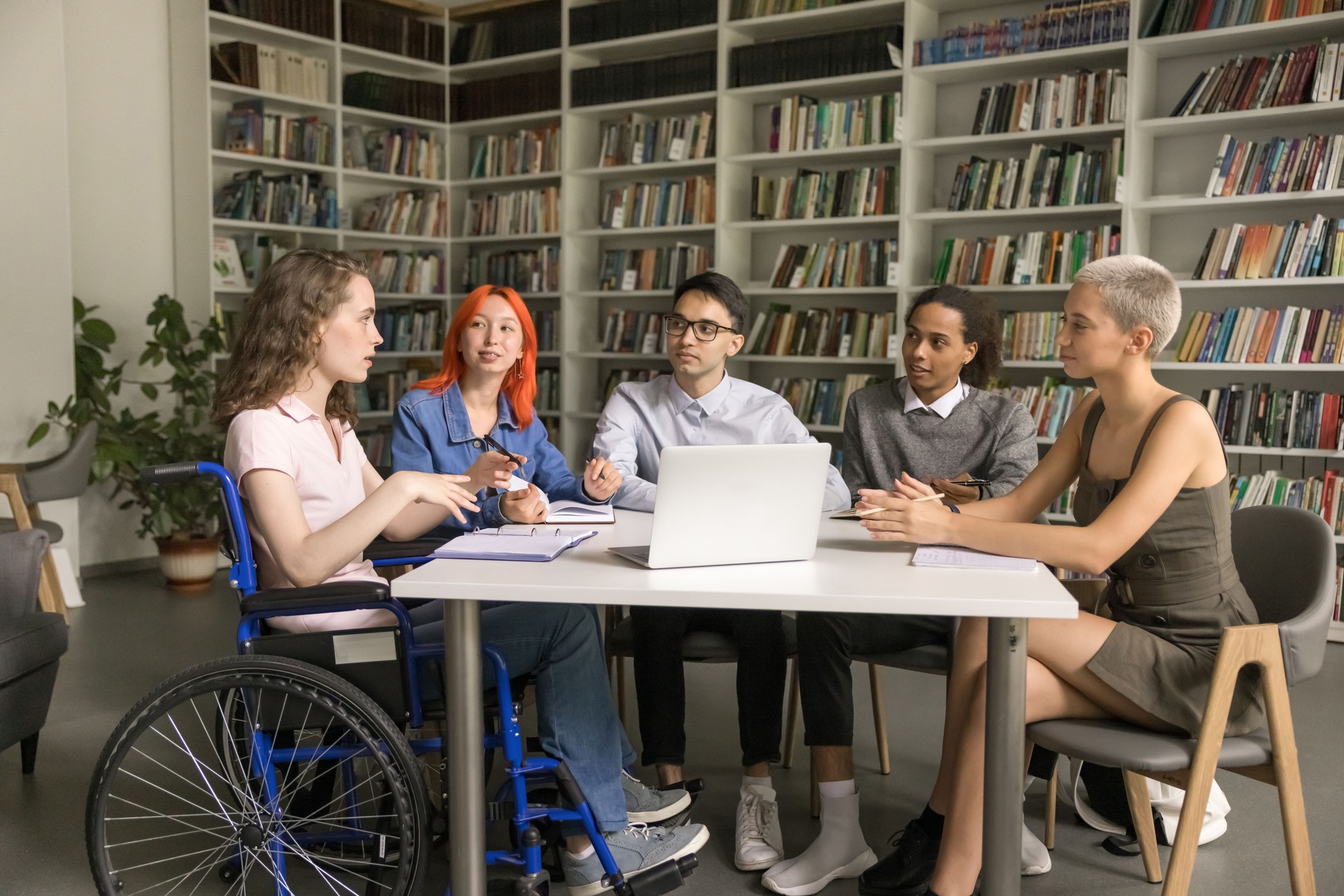 Multiethnic team of students inclusively classmate with disability studying together